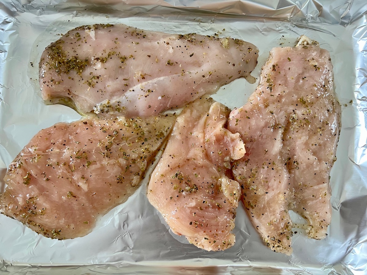 Four raw seasoned chicken cutlets on an aluminum lined sheet pan for Chicken Ricotta Pasta Recipe.