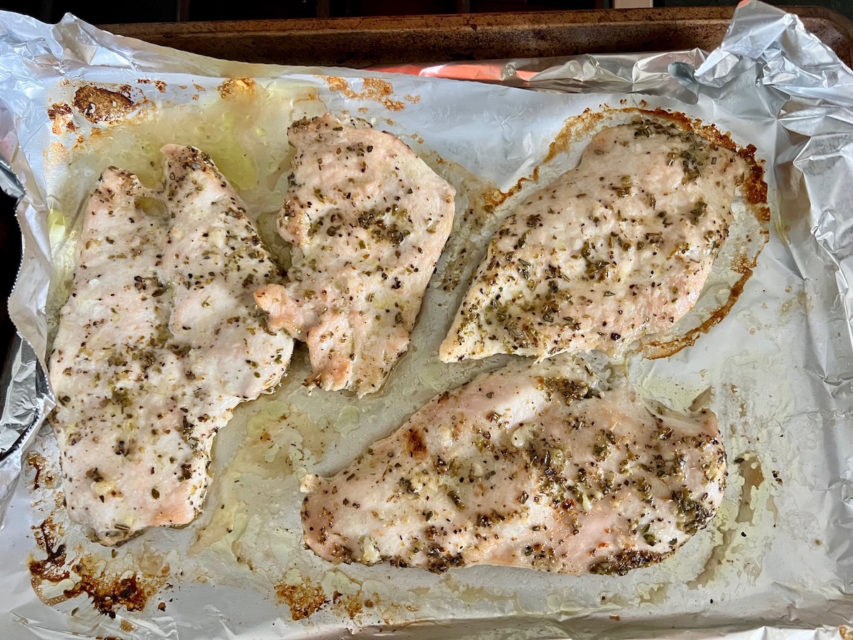Four cooked seasoned chicken cutlets on an aluminum lined sheet pan for Chicken Ricotta Pasta Recipe.