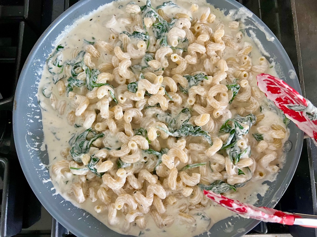 Pasta being mixed into the ricotta sauce in a pan with tongs for Chicken Ricotta Pasta Recipe.