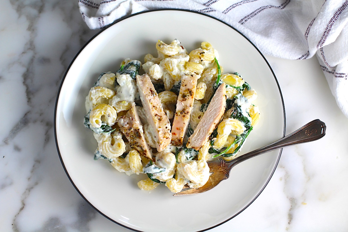 Chicken Ricotta Pasta on a plate with fork with spinach cooked and mixed in with the pasta and the chicken sliced and laying on top.