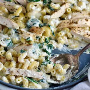 Chicken Ricotta Pasta being scooped with a spoon in a large frying pan with spinach cooked and mixed in and the chicken sliced and laying on top.