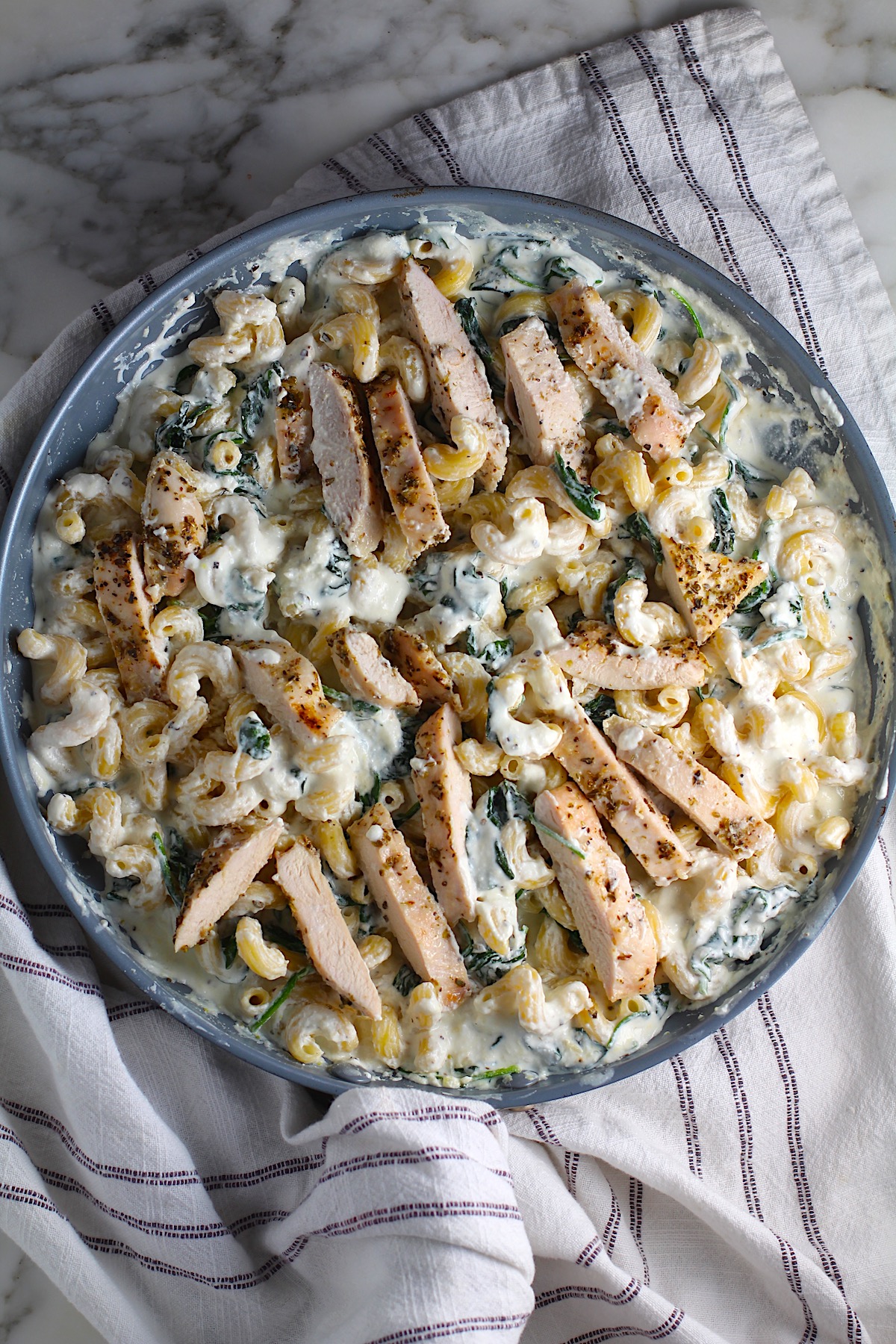 Chicken Ricotta Pasta in a large frying pan with spinach cooked and mixed in and the chicken sliced and laying on top.