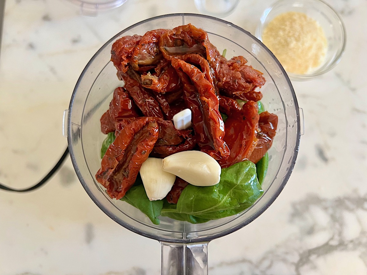 Basil leaves, sun dried tomatoes, garlic, and oil added to a food processor before being blended for Sun Dried Tomato Pesto Pasta.