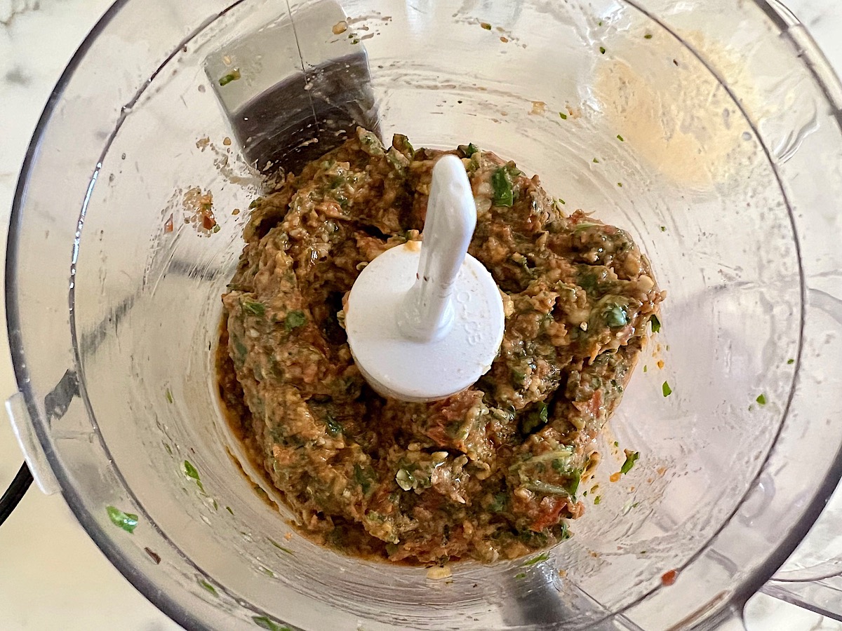 Looking top down inside a food processor at blended Sun Dried Tomato Pesto.