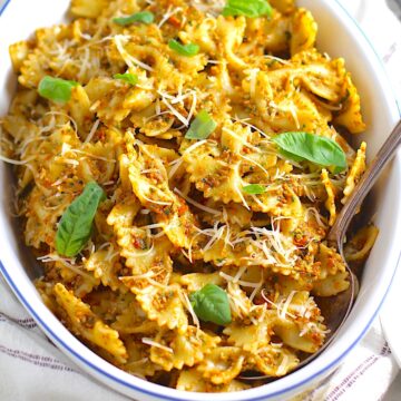 Sun Dried Tomato Pesto Pasta in an oval serving platter with serving spoon on a blue and white striped towel on the counter.
