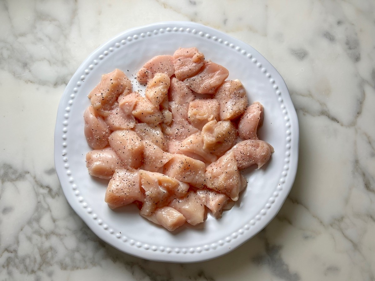 Raw chicken cut into cubes on a white plate on counter for Creamy Sun Dried Tomato Sauce with Chicken and Pasta recipe.