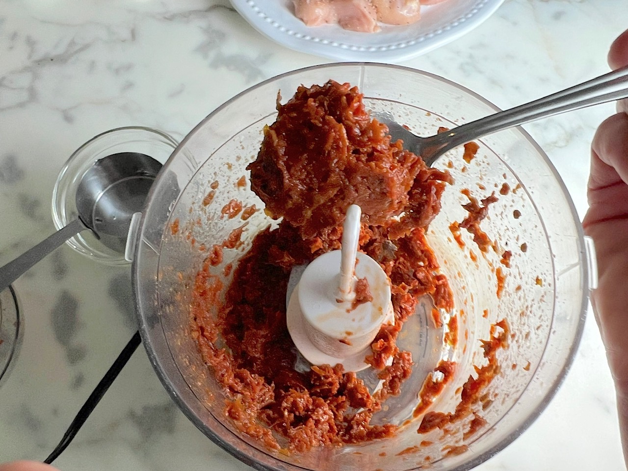 Spoon scooping pureed sun dried tomatoes in a mini food processor for Creamy Sun Dried Tomato Sauce with Chicken and Pasta recipe.