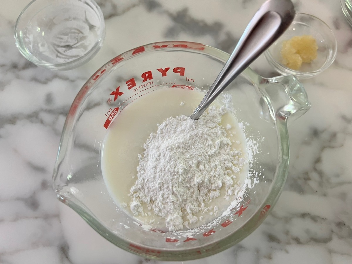 Cornstarch added (but not mixed in) to half and half in a measuring cup with a spoon for Creamy Sun Dried Tomato Sauce with Chicken and Pasta recipe.