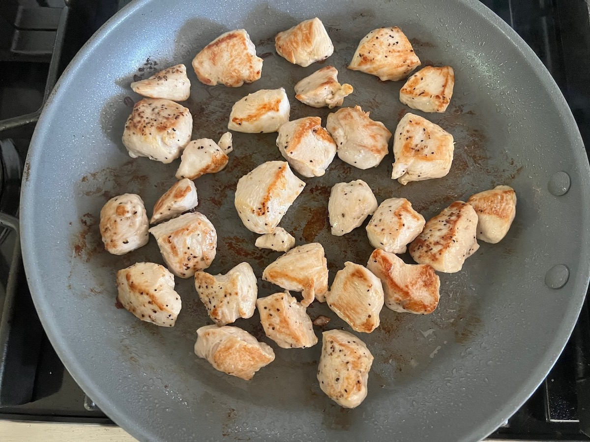 Browned chicken cubes in a pan on stove for Creamy Sun Dried Tomato Sauce with Chicken and Pasta recipe.