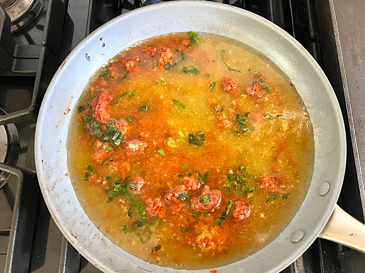 Pureed sun dried tomatoes, broth, basil, and garlic added to a large pan on store for the Creamy Sun Dried Tomato Sauce with Chicken and Pasta recipe.