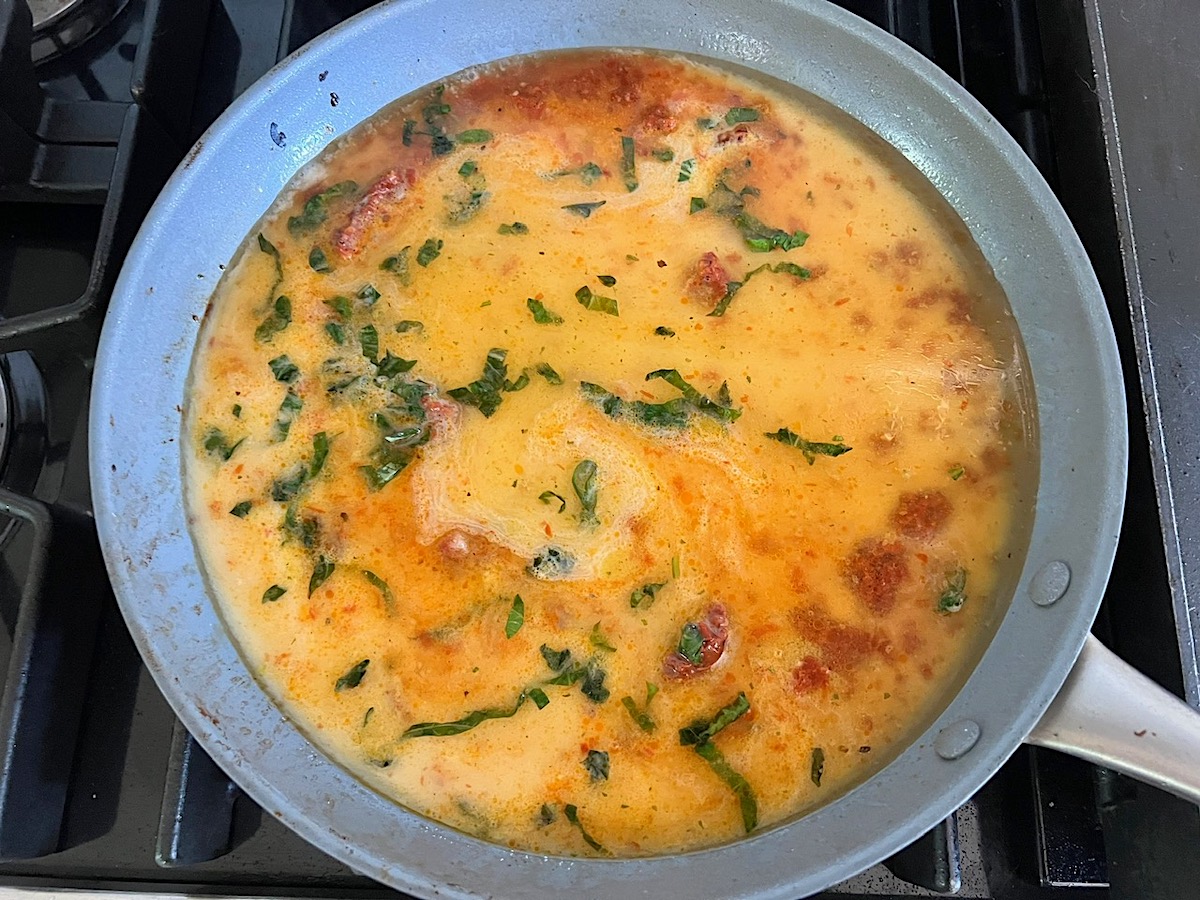 Cornstarch slurry with half and half added to the sun dried tomato sauce in a large pan on stove for the Creamy Sun Dried Tomato Sauce with Chicken and Pasta recipe.