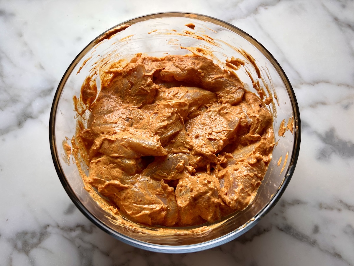 Raw chicken strips in a clear glass bowl mixed with Tikka yogurt marinade for the Chicken Tikka Wraps.
