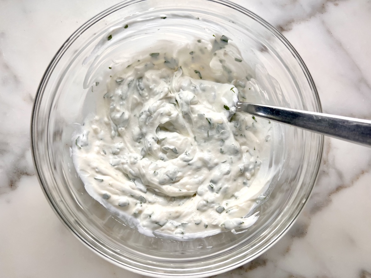 Cilantro Yogurt sauce in a clear glass bowl with a fork for the Chicken Tikka Wraps.