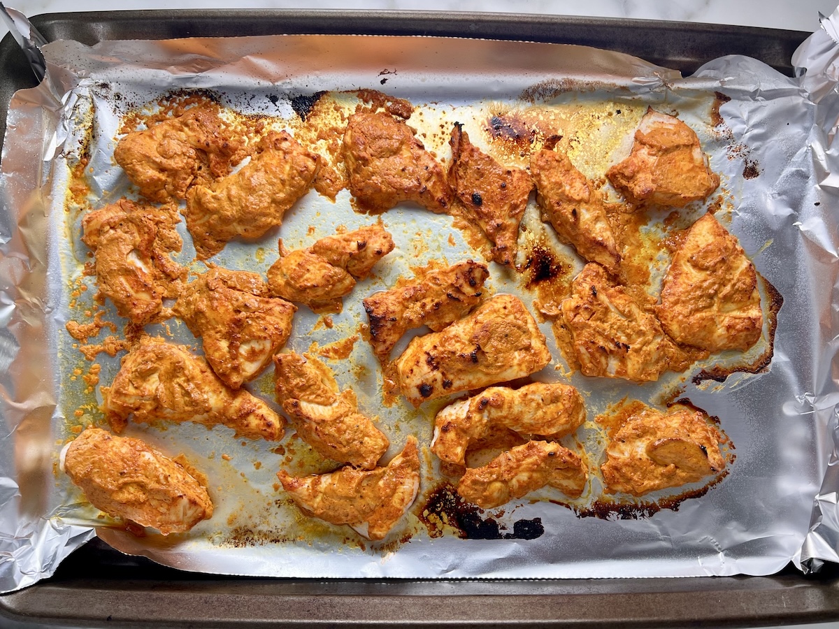 Chicken Tikka browned and roasted with some charred bits on a foil-lined pan for the Chicken Tikka Wraps.