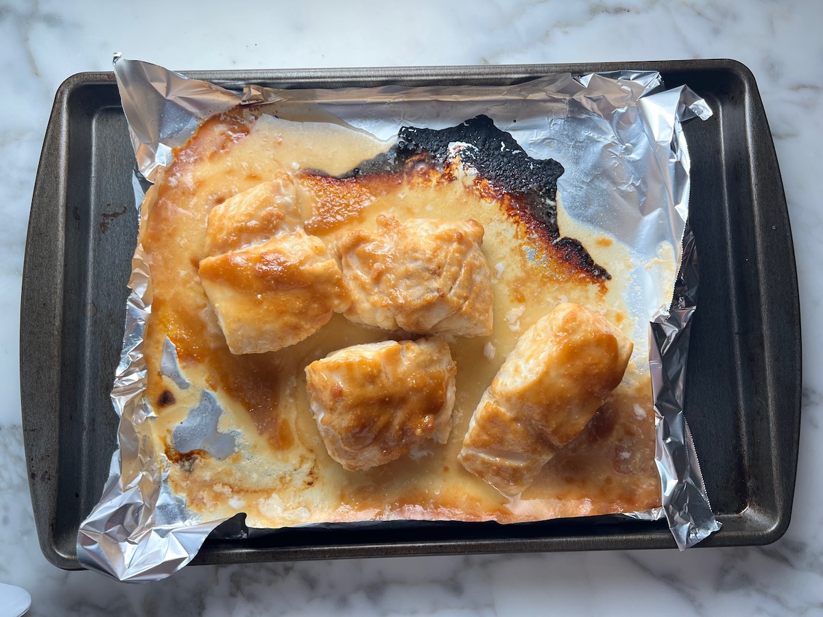 Four cooked cod fillets with golden brown miso glaze on an aluminum lined sheet pan for the Glazed Miso Cod Recipe.