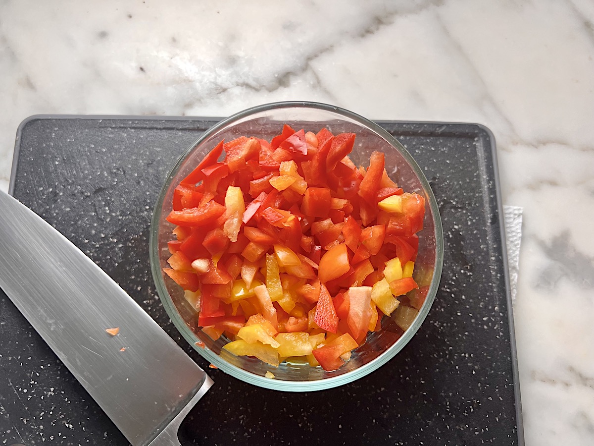 Dice red and yellow bell pepper tops in a bowl on black cutting board with knife sitting next to it for Stuffed Peppers with Ground Turkey recipe.