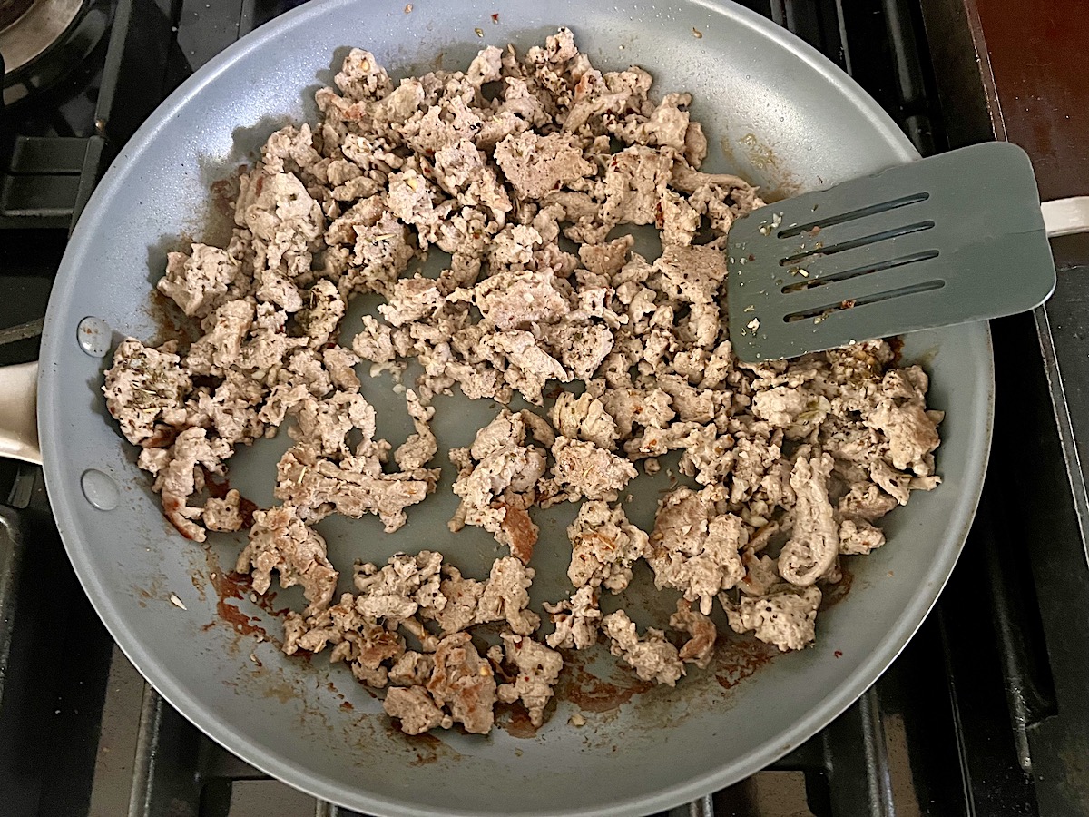 Ground turkey cooking in a frying pan with spatula on the stove for the Stuffed Peppers with Ground Turkey recipe.