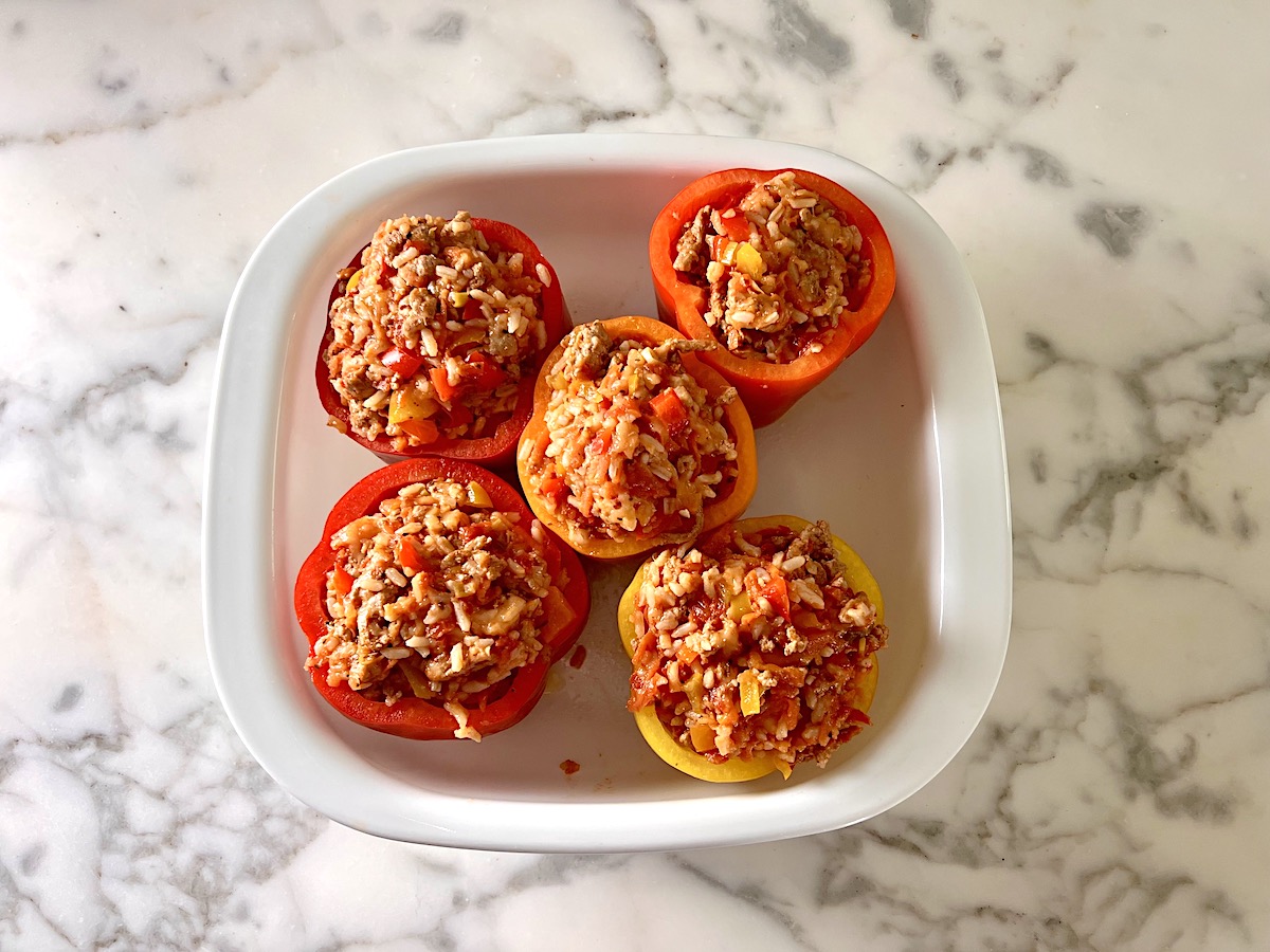 Five Red and Yellow peppers stuffed with with Ground Turkey and rice filling in the large square casserole dish on the counter for Stuffed Peppers with Ground Turkey recipe.