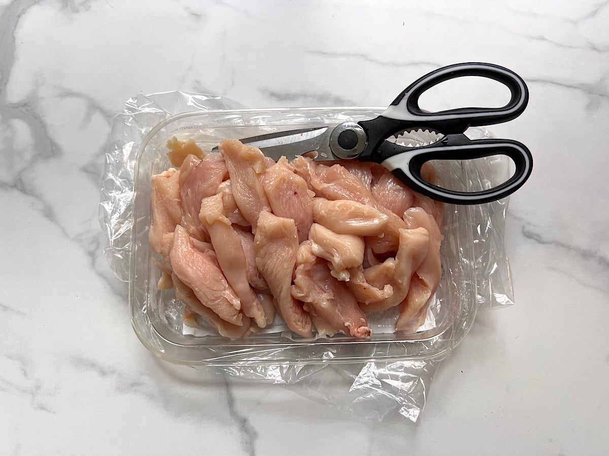 Raw chicken breast cut into strips with cooking scissors in the package on the counter for this Chicken Stir Fry Recipe.