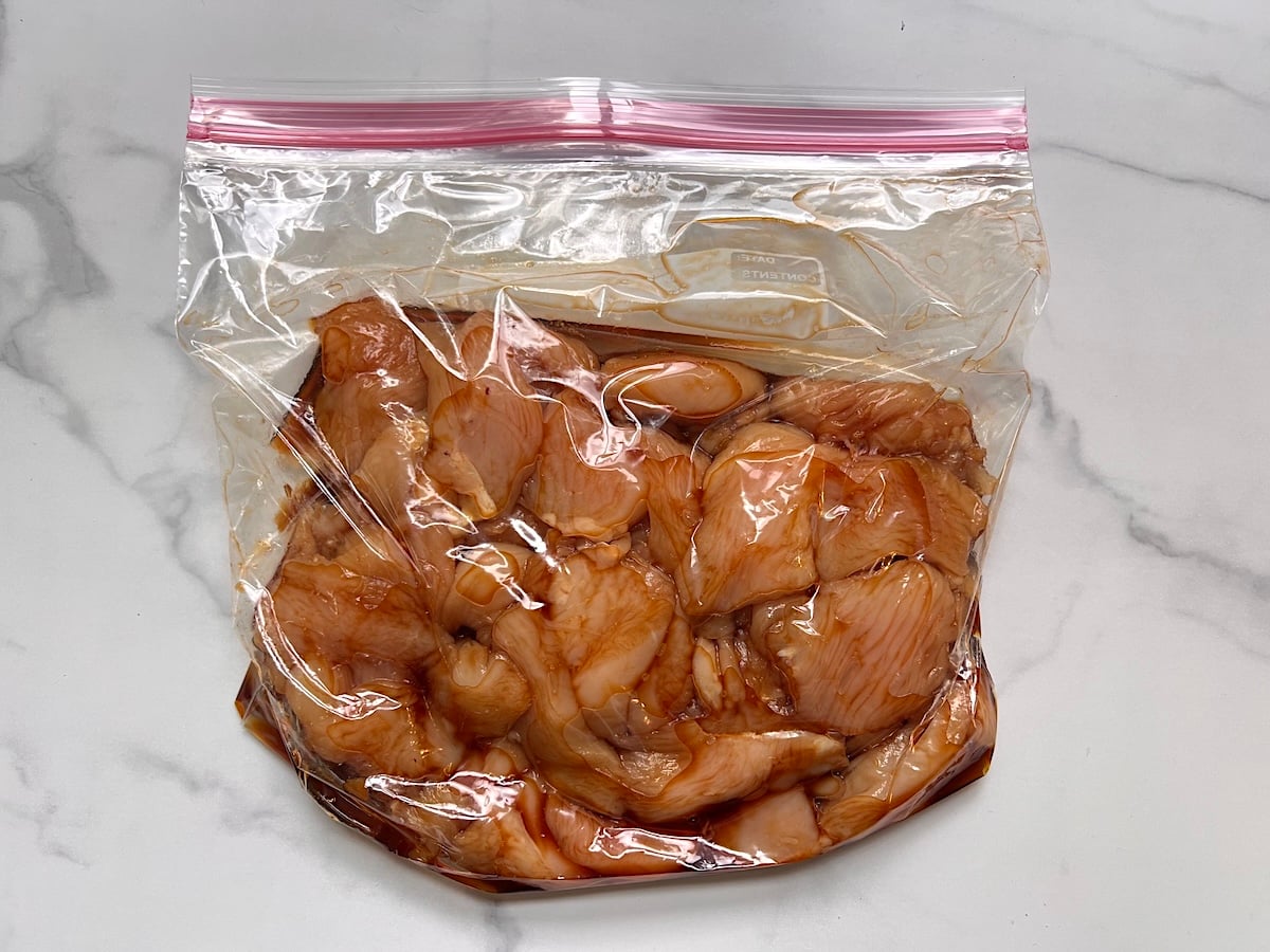 Raw chicken breast cut into strips in a storage bag marinating with soy sauce on the counter for this Chicken Stir Fry Recipe.