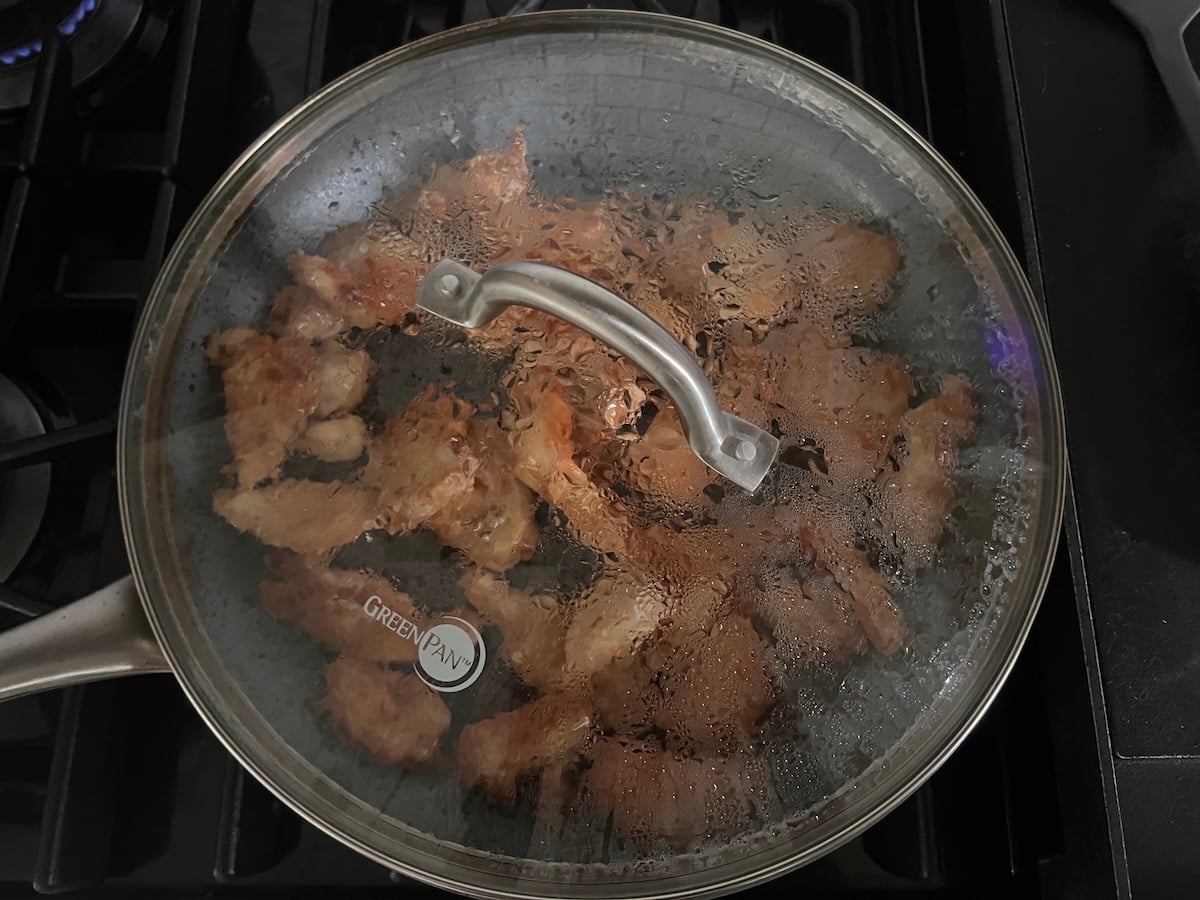 Clear glass cover over top of chicken strips cooking in a skillet on stove for this Chicken Stir Fry Recipe.
