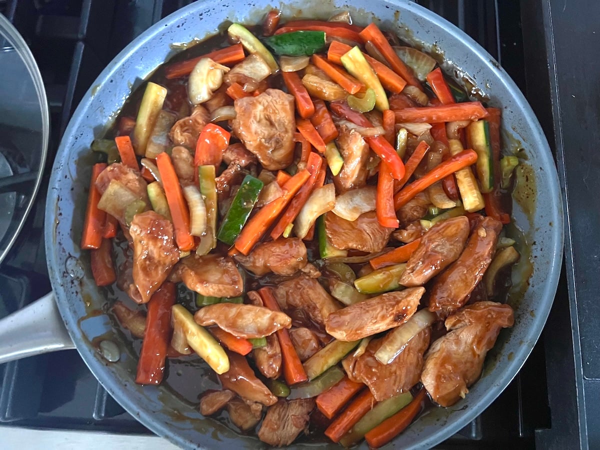 Chicken Stir Fry cooking in the skillet with sauce, sliced zucchini, red pepper, celery, onions, and carrots .