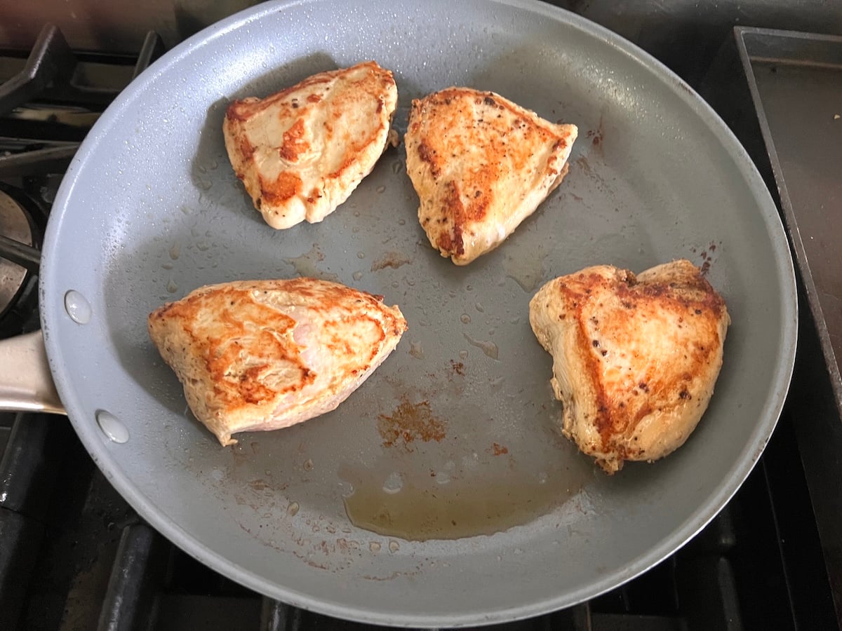 4 pieces of boneless, skinless chicken breast seared in a pan with seared side-up and browned bits on the bottom of pan still on the stove for this Chicken au Poivre recipe.