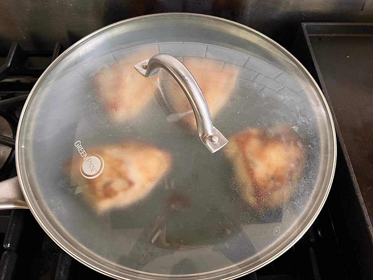 4 pieces of boneless, skinless chicken breast seared in a pan with the clear lid on top still on the stove for this Chicken au Poivre recipe.