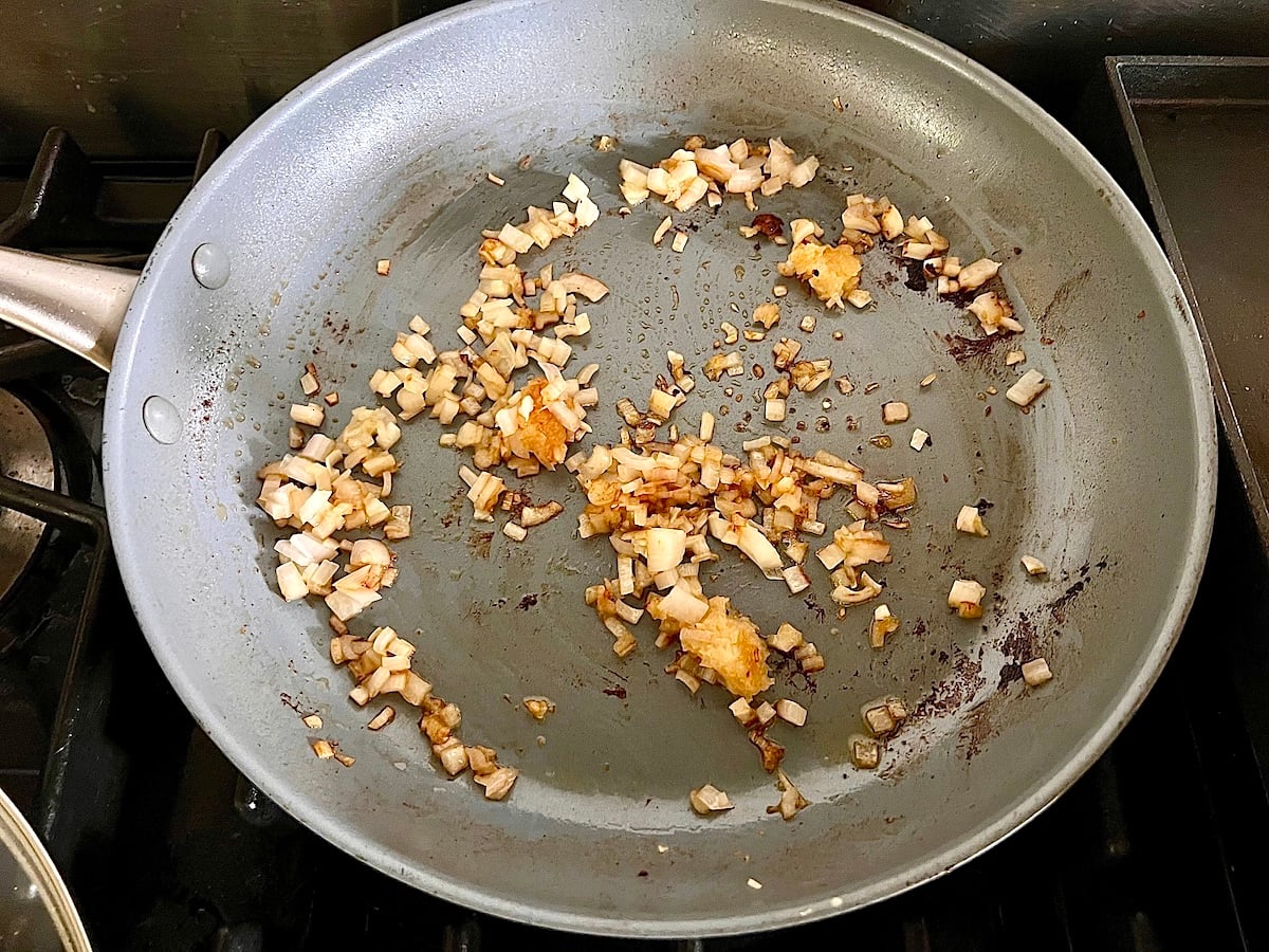 Finely diced shallots cooking and browning in the pan after the chicken is transferred out for this Chicken au Poivre recipe.