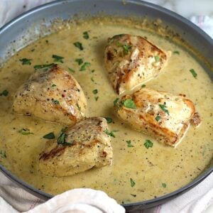 4 pieces of chicken breast seared and cooking in a creamy brown sauce in a pan with seared side-up and browned bits on the bottom of pan still on the stove for this Chicken au Poivre recipe.