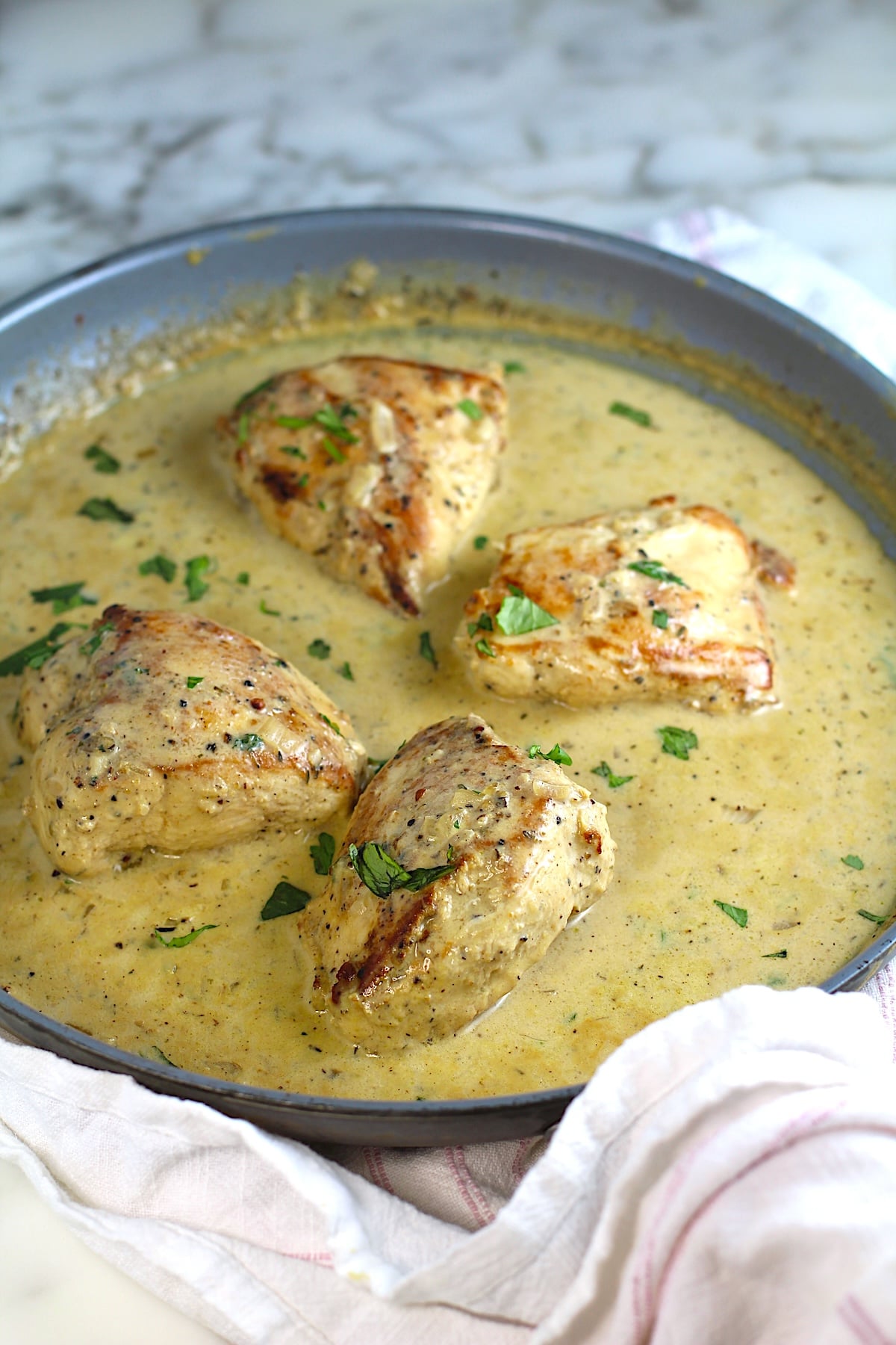 4 pieces of chicken breast seared and cooking in a creamy brown sauce in a pan with seared side-up and browned bits on the bottom of pan still on the stove for this Chicken au Poivre recipe.