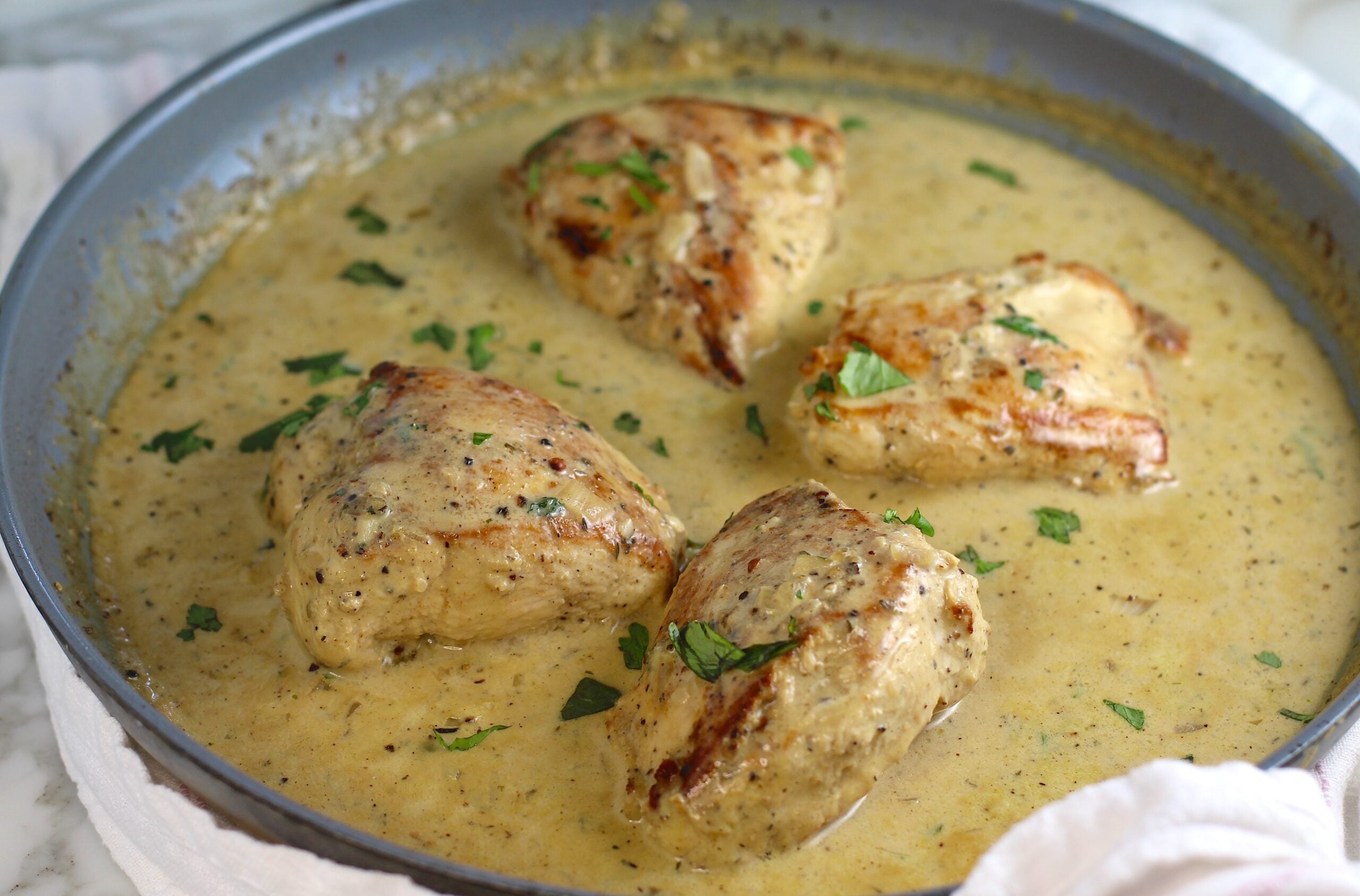 4 pieces of chicken breast seared and cooking in a creamy brown sauce in a pan with seared side-up and browned bits on the bottom of pan still on the stove for this Chicken au Poivre recipe.