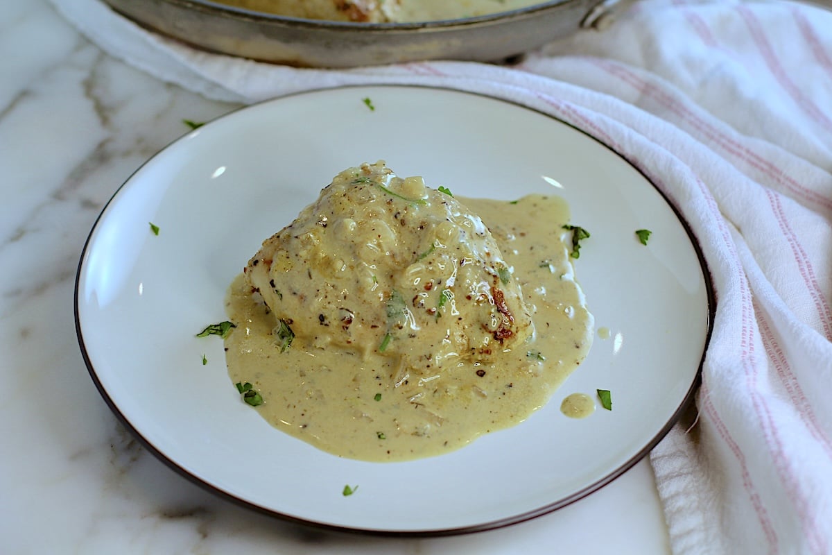 Half of a chicken breast on a plate covered in a creamy peppercorn sauce for this Chicken au Poivre recipe.