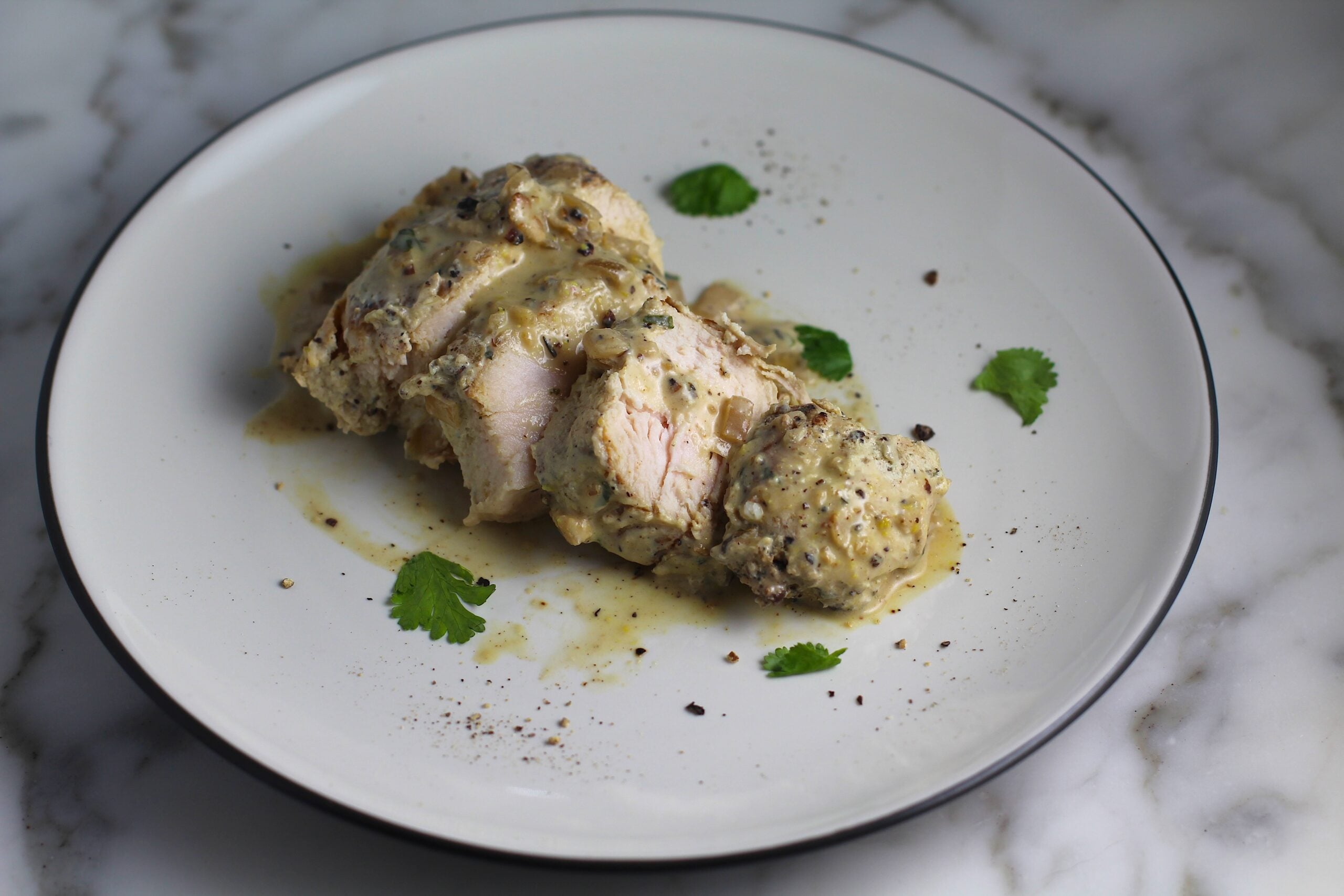 Piece of chicken breast sliced and fanned out on a plate with the au poivre sauce poured over top and more fresh ground black pepper on top and on the plate along with fresh parsley leaves for this Chicken au Poivre recipe.