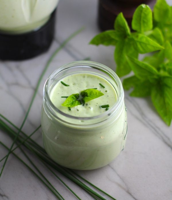 Basil & Chive Yogurt Dressing in a jar on counter with basil leaves and chives on top and on the counter. This dressing with Lemon and Honey is creamy, light, savory, and a little bit sweet. It takes only minutes to make this delicious homemade dressing.  Basil & Chive Yogurt Dressing is perfect for salads, for drizzling over roasted veggies, steak, chicken, or fish, and amazing for dipping fries into!!