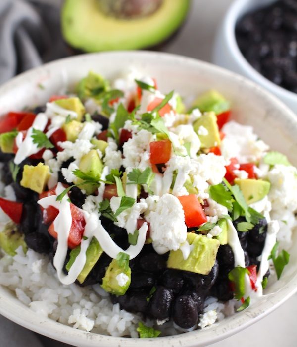 Black Bean Taco Bowl with rice, smoky black beans, avocado, salty Cotija cheese, sour cream, fresh tomato, and bright cilantro. This Black Bean Taco Bowl Bar lets everyone fills their bowl with any of the toppings they want! Perfect for kids. #tacos #tacobowls #healthyfood #dinner #healthydinner #familydinner #kidsdinner #blackbeans #vegetarian