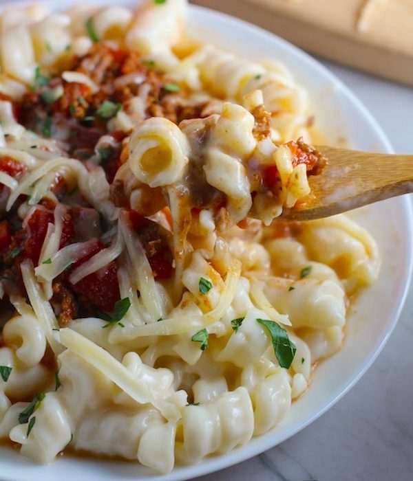 Chili Mac and Cheese on a plate with fork. This Recipe has creamy and cheesy pasta topped with smokey, tangy, savory beef chili! #macandcheese #chilirecipes