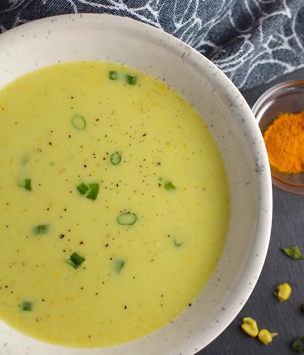 Closeup of Chilled Golden Corn Soup in a bowl with turmeric spice in a bowl on the side. Scallions on top for garnish. It's thick, creamy, silky and delicious.  The entire family will love this easy stovetop corn soup! #summerfood #cornsoup #corn #vegetarian #vegetablerecipes #sides