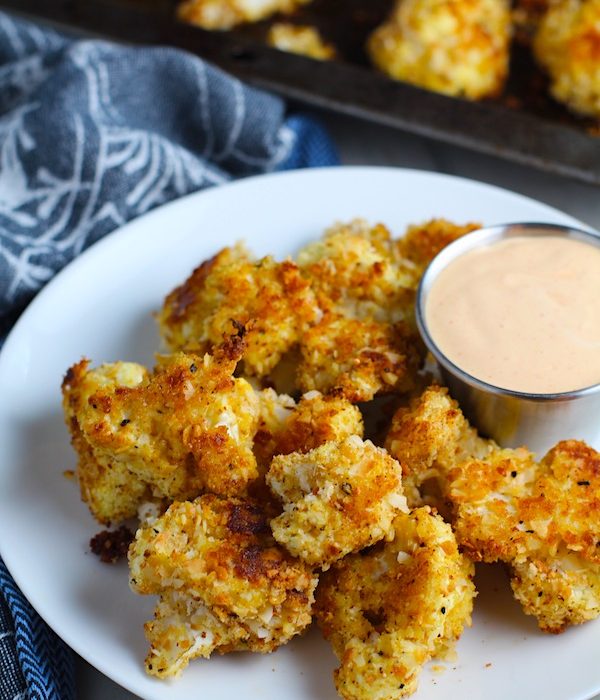 Baked Coconut Cauliflower Bites on plate with Sriracha Mayo dipping sauce.  They have a slightly sweet and salty crunch outside from the shredded coconut and panko mixture.  The inside is soft and creamy.  Dip in the Sriracha Mayo. 