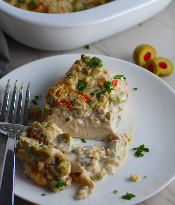 Creamy Olive Chicken cut on plate with fork and casserole dish in background. This is magnificently thick and creamy and infused with garlic flavor and nuttiness from the Parmesan. The best part; however, is the salty and briny flavor kick from the green olives with a little sweetness from the pimiento. #chicken #chickenrecipes #chickendinner #easydinners #easyrecipes #comfortfood #casserole