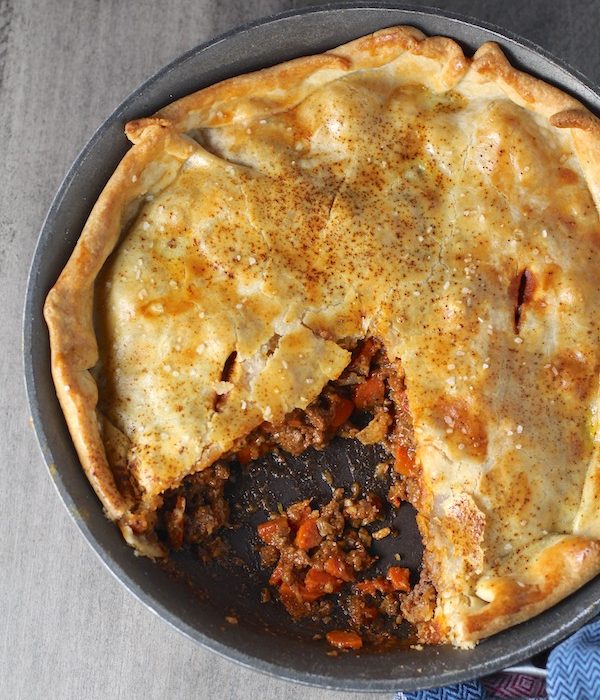 Flaky Empanada Pie with Ground Beef Recipe in a skillet with a piece out on counter. It has a perfect flaky, buttery pastry on the outside with a savory, smokey, salty ground beef filling.  The best part is that everything cooks in one skillet!