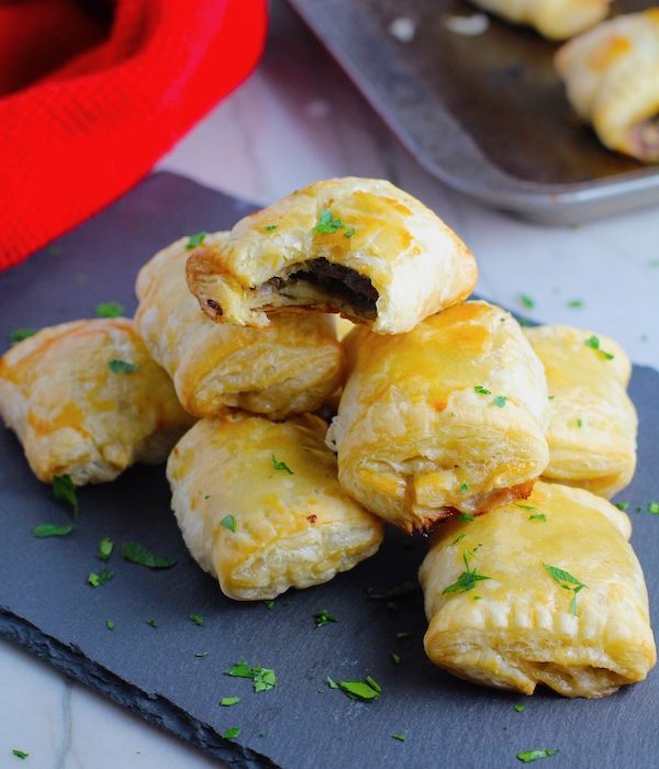 Mini Beef Wellington Bites stacked on platter. They are flaky and buttery on the outside. Puff Pastry is filled with a creamy mushroom and parmesan filling and tender beef filet.  #appetizers #partyfood