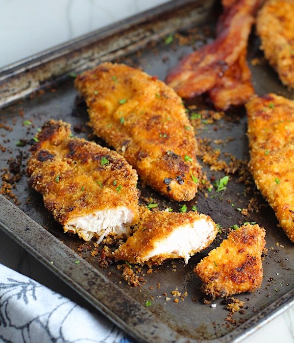 Oven Fried Chicken Breast cut on pan with bacon in background. The chicken is coated with Bacon Crumbs and Honey and it's healthier because it's baked, not fried, but still gives you all of the crispy, crunchy goodness!  It also gives you sweet and salty crunch with the addition of honey and bacon!