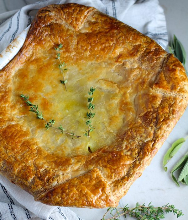 Puff Pastry Turkey Pot Pie in a casserole dish with fresh thyme on top and fresh sage on the counter. It's an easy dinner recipe to use leftover turkey from the holidays and ingredients you can have on hand!
