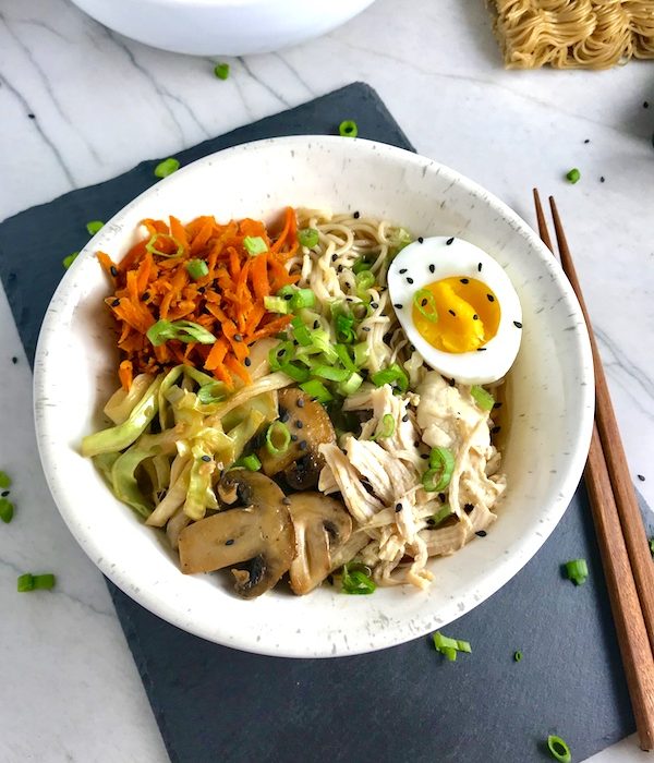 Healthy Chicken Ramen Noodles with Chicken, carrots, cabbage, half of a hard boiled egg, scallions, and black sesame seeds with chopsticks on the side.