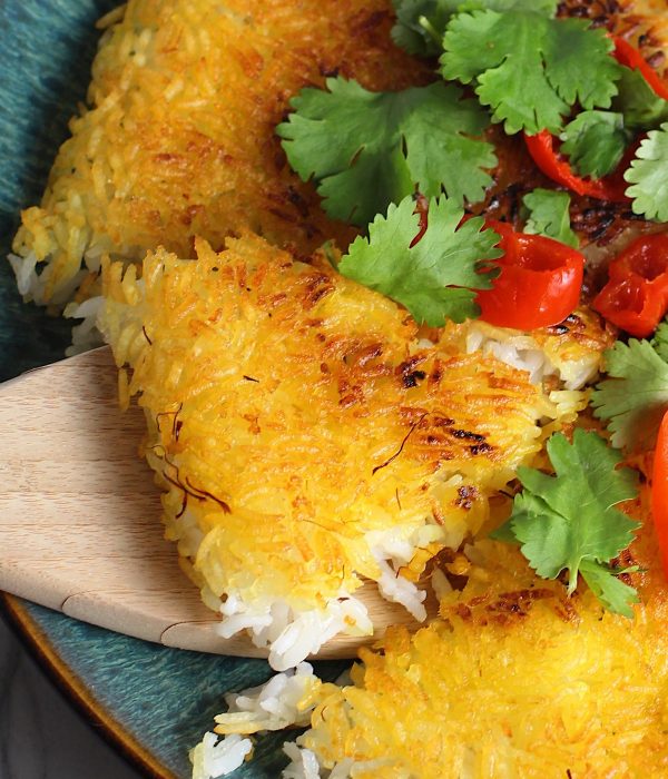 Saffron Butter Crispy Rice on a plate with cilantro and peppadew peppers on top. Spatula scooping up a triangle piece. Saffron brings a floral note and beautiful yellow-orange color.  Added to the butter is what gives this crispy rice the buttery, crispy bottom.