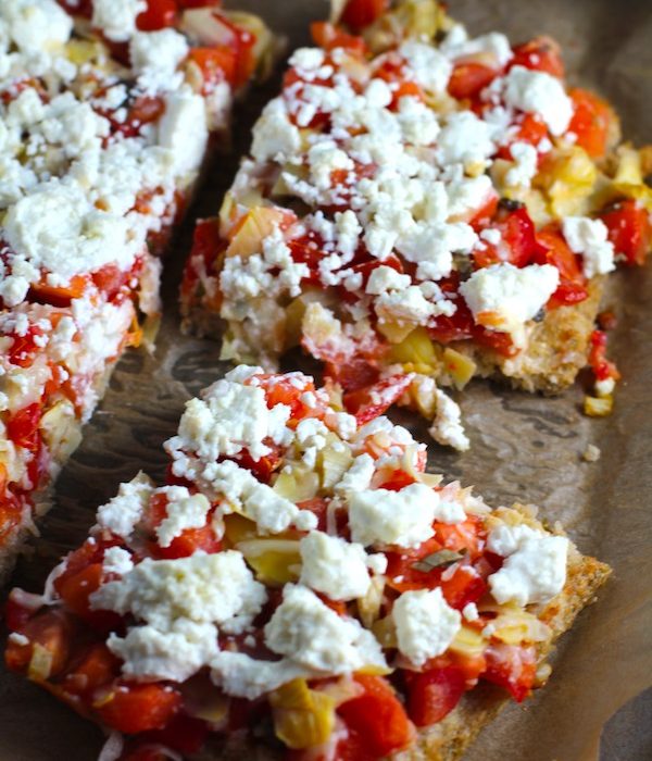 Close up of cut Tomato Tart on parchment. It gives you crunch from the Quinoa crust, a burst of fresh from the tomatoes, tons of flavor from the basil and garlic, tang and meatiness from the artichoke and so much creaminess from the mozzarella and goat cheese!  It's addictive and delicious!